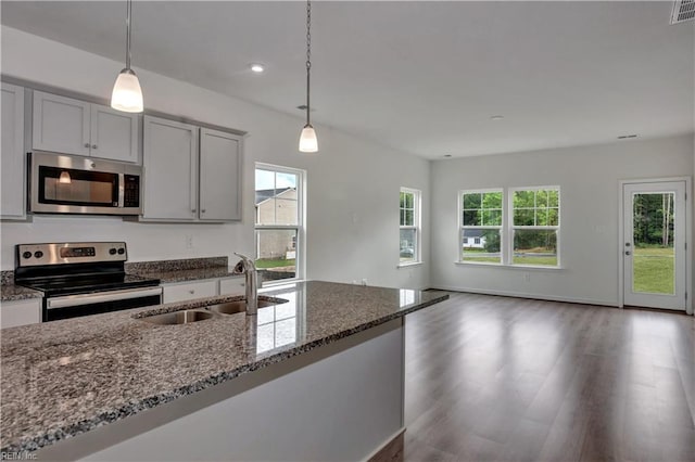 kitchen featuring dark stone counters, gray cabinets, a sink, stainless steel appliances, and open floor plan