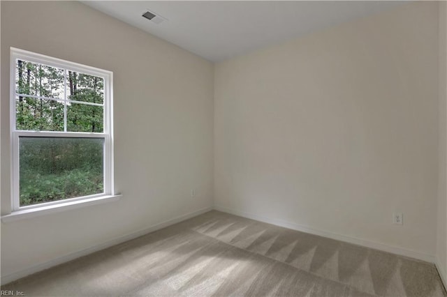 empty room featuring a wealth of natural light, visible vents, light carpet, and baseboards