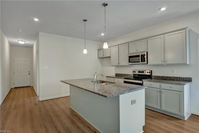 kitchen featuring dark stone counters, a sink, an island with sink, light wood-style floors, and stainless steel appliances