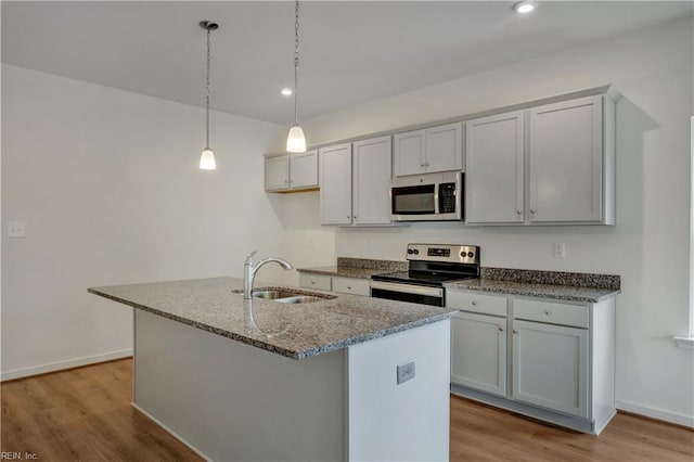 kitchen with light wood finished floors, dark stone counters, an island with sink, stainless steel appliances, and a sink