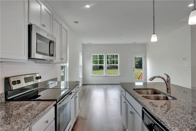 kitchen with a sink, stainless steel appliances, white cabinets, light wood finished floors, and hanging light fixtures