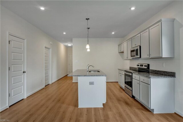 kitchen with a kitchen island with sink, light wood-style flooring, a sink, dark stone countertops, and stainless steel appliances