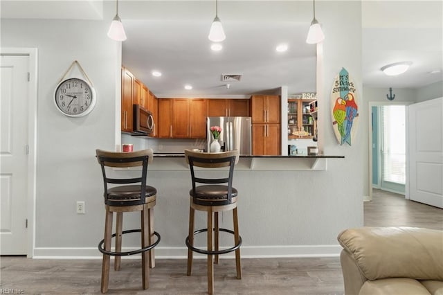 kitchen featuring appliances with stainless steel finishes, pendant lighting, wood-type flooring, and a breakfast bar