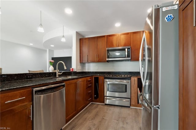 kitchen with light hardwood / wood-style floors, pendant lighting, dark stone counters, sink, and appliances with stainless steel finishes