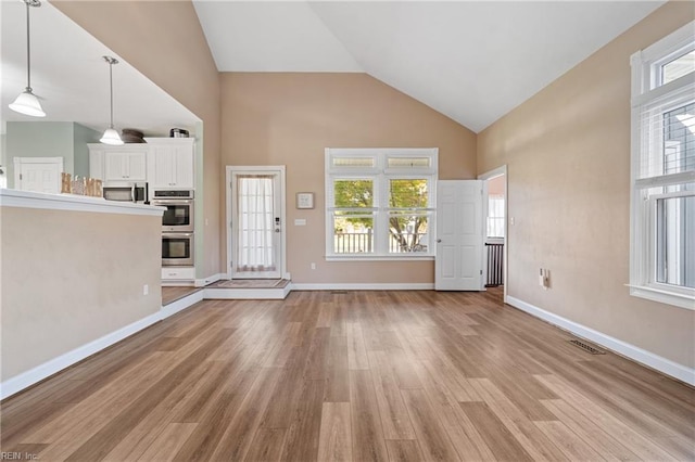 unfurnished living room with high vaulted ceiling, light hardwood / wood-style flooring, and a healthy amount of sunlight