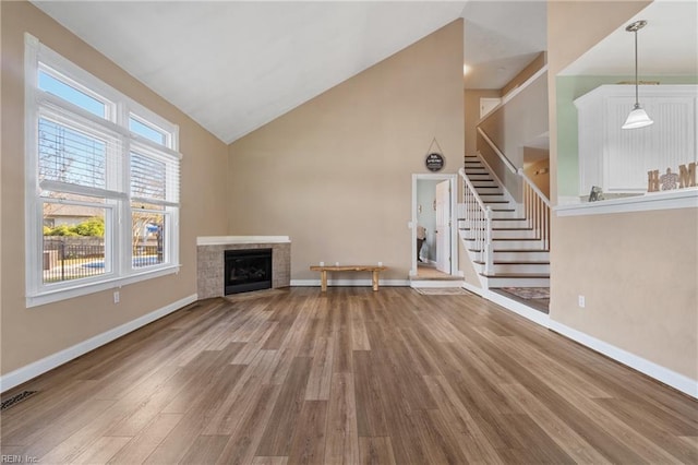 unfurnished living room with wood-type flooring, high vaulted ceiling, and a tiled fireplace