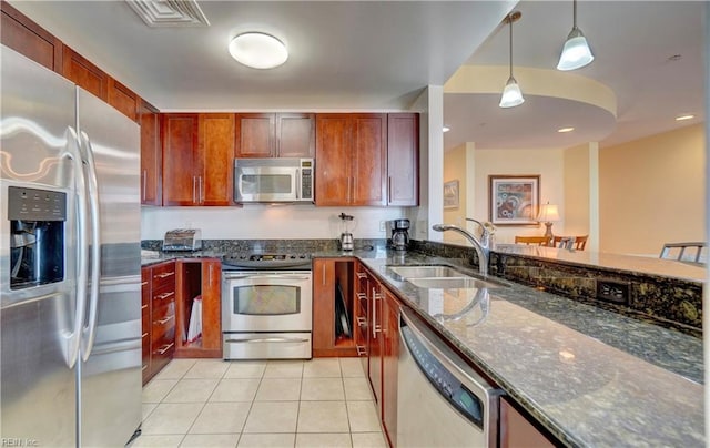 kitchen with appliances with stainless steel finishes, sink, decorative light fixtures, dark stone counters, and light tile patterned floors