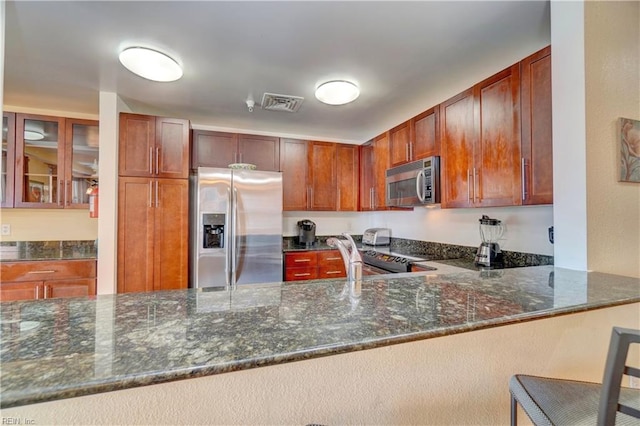 kitchen featuring a kitchen breakfast bar, appliances with stainless steel finishes, kitchen peninsula, and dark stone counters