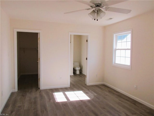 unfurnished bedroom featuring a walk in closet, ensuite bathroom, ceiling fan, dark wood-type flooring, and a closet