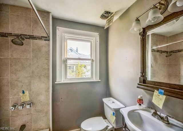 bathroom with a tile shower, sink, and toilet