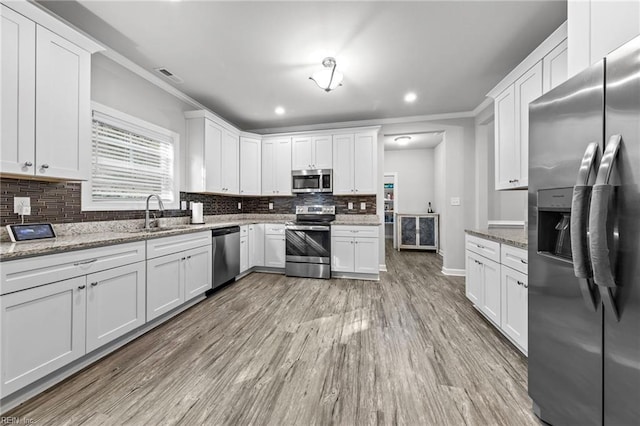 kitchen featuring appliances with stainless steel finishes, light stone counters, white cabinetry, crown molding, and light hardwood / wood-style flooring