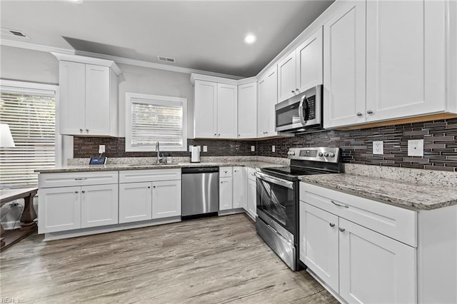 kitchen with appliances with stainless steel finishes, sink, light stone counters, white cabinets, and crown molding