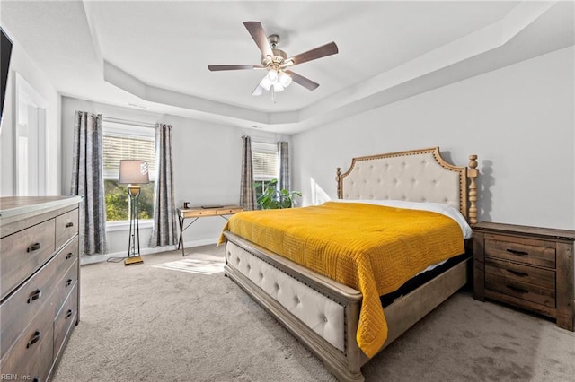 bedroom with multiple windows, a tray ceiling, light colored carpet, and ceiling fan