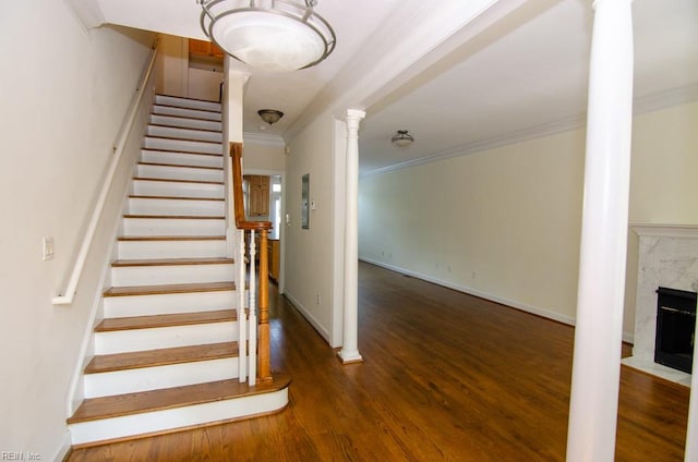 staircase featuring a premium fireplace, crown molding, ornate columns, and hardwood / wood-style flooring