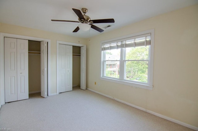 unfurnished bedroom with multiple closets, light carpet, and ceiling fan