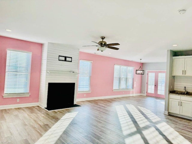 unfurnished living room featuring light hardwood / wood-style flooring, sink, a fireplace, and ceiling fan with notable chandelier