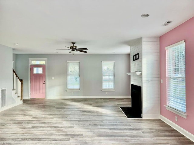 unfurnished living room with light hardwood / wood-style flooring, a large fireplace, and ceiling fan