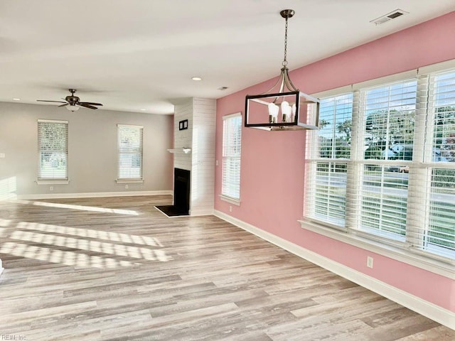 interior space featuring a large fireplace, light hardwood / wood-style floors, ceiling fan with notable chandelier, and a healthy amount of sunlight