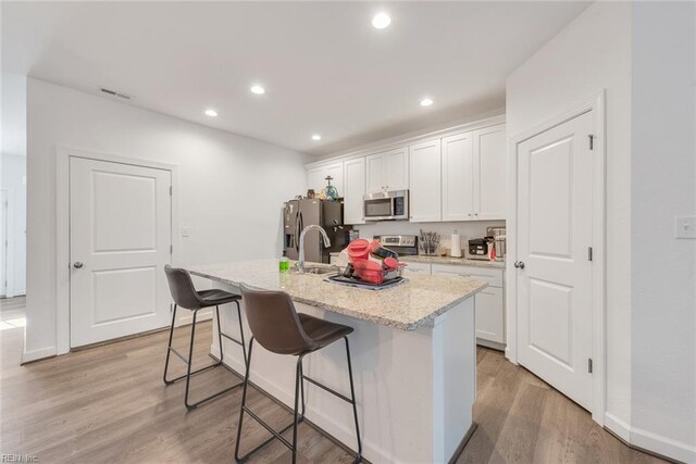 kitchen featuring white cabinetry, light wood-type flooring, stainless steel appliances, and an island with sink