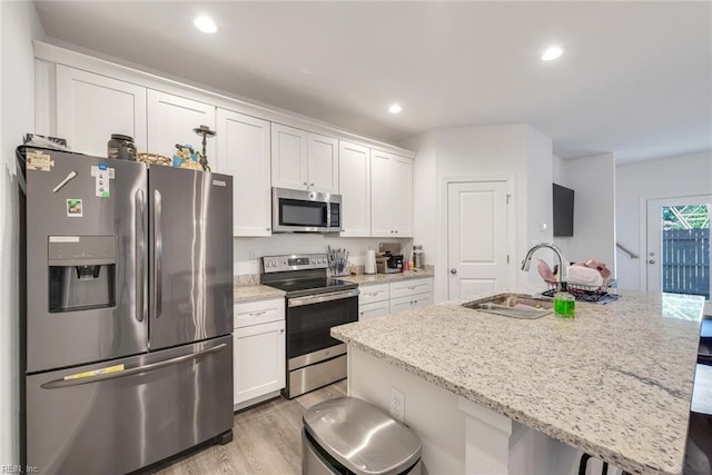 kitchen with a center island with sink, white cabinets, light stone counters, and stainless steel appliances