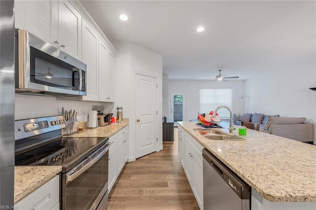 kitchen with appliances with stainless steel finishes, sink, light hardwood / wood-style floors, white cabinets, and a center island with sink