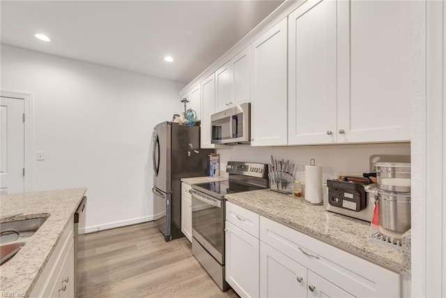 kitchen with light stone counters, white cabinetry, stainless steel appliances, and light wood-type flooring