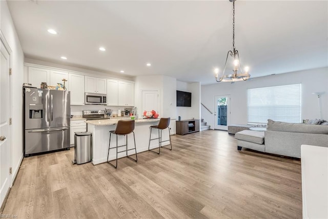 kitchen with a kitchen breakfast bar, light hardwood / wood-style floors, stainless steel appliances, white cabinets, and a kitchen island with sink