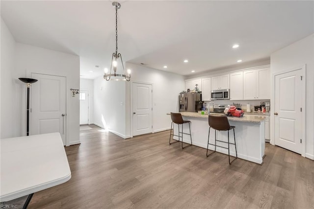 kitchen with white cabinets, an island with sink, a breakfast bar, hardwood / wood-style flooring, and stainless steel appliances