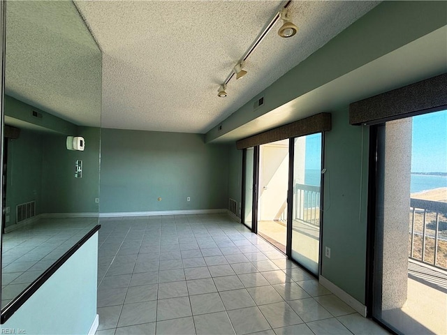 empty room featuring light tile patterned flooring, a textured ceiling, track lighting, and a water view