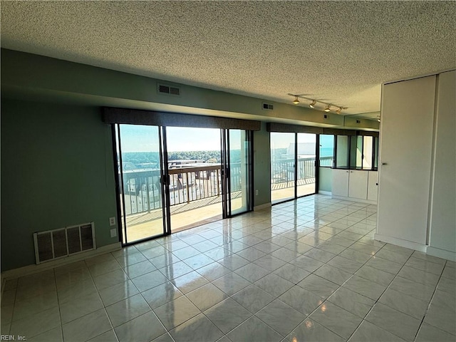 unfurnished room with a wealth of natural light, a textured ceiling, rail lighting, and light tile patterned floors