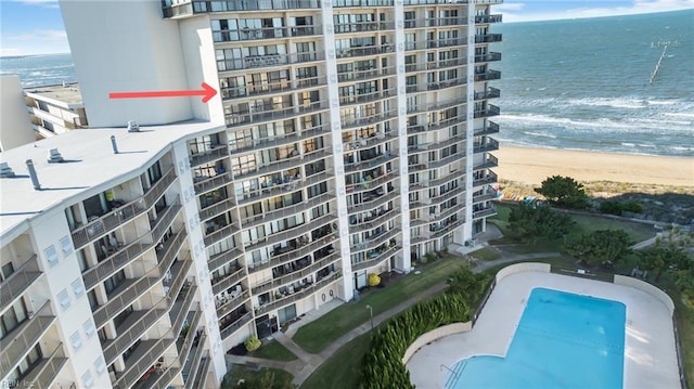 view of building exterior with a view of the beach, a community pool, and a water view