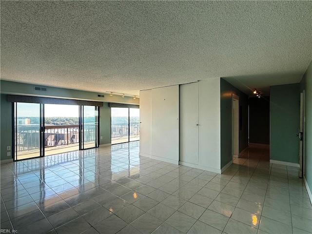 unfurnished room with a textured ceiling, tile patterned floors, and rail lighting