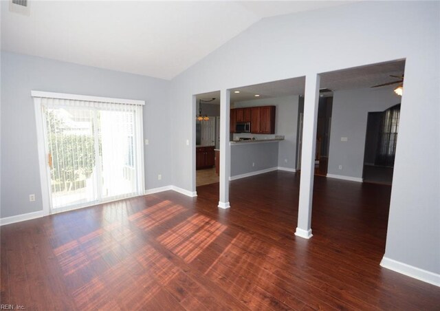 unfurnished living room featuring vaulted ceiling, ceiling fan with notable chandelier, and dark hardwood / wood-style flooring