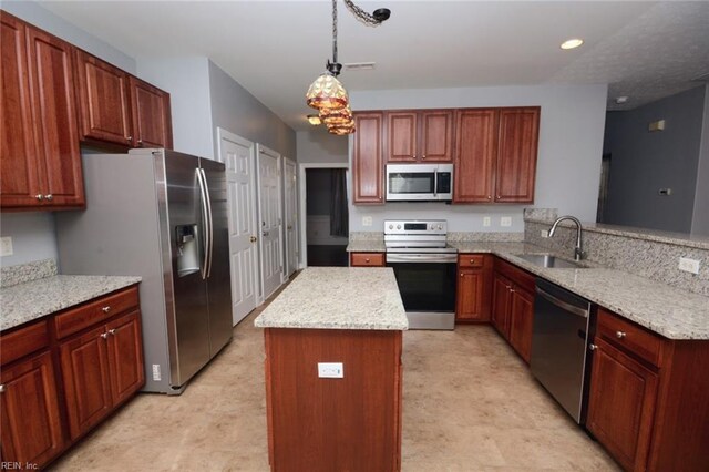 kitchen featuring light stone counters, a kitchen island, stainless steel appliances, sink, and decorative light fixtures