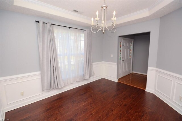 spare room featuring a notable chandelier, ornamental molding, a tray ceiling, and dark wood-type flooring