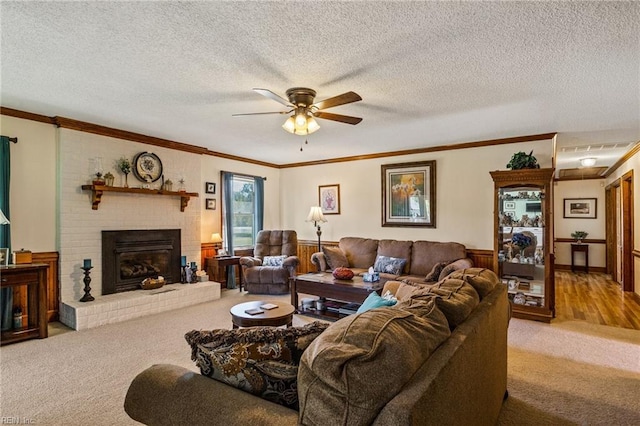 carpeted living room featuring ceiling fan, a textured ceiling, ornamental molding, and a fireplace