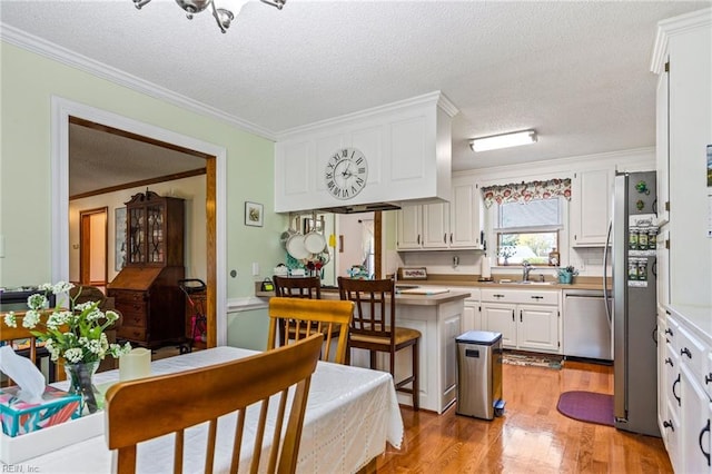 kitchen with a textured ceiling, light hardwood / wood-style floors, stainless steel appliances, white cabinets, and crown molding