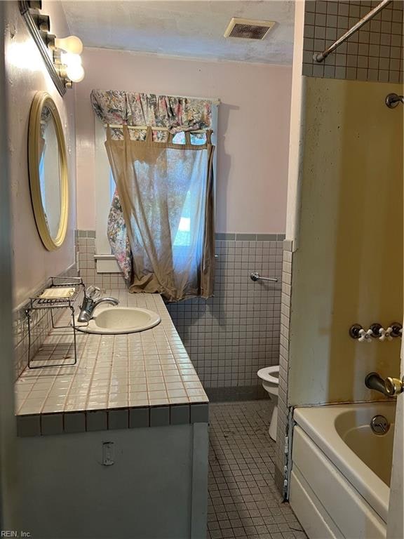 full bathroom with toilet, tile patterned floors, tile walls, vanity, and tiled shower / bath combo