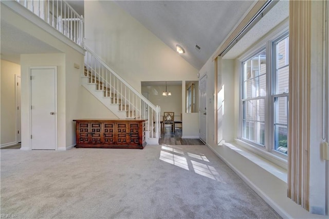 entrance foyer featuring a notable chandelier, high vaulted ceiling, a healthy amount of sunlight, and carpet floors