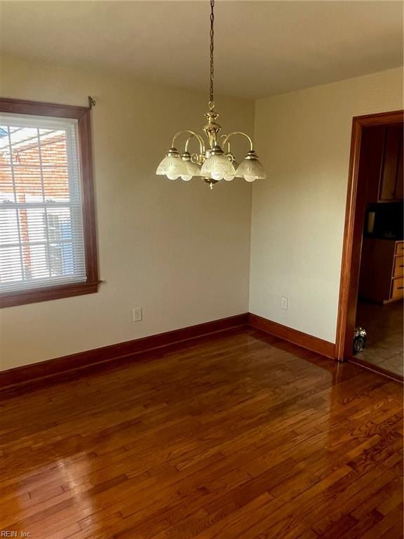 spare room featuring dark wood-type flooring and a notable chandelier