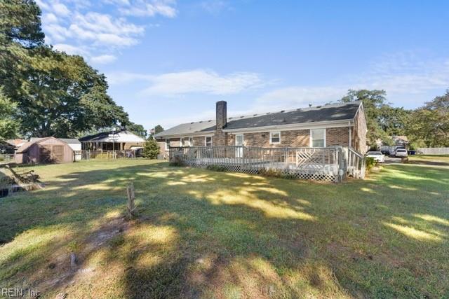 back of house with a storage shed, a wooden deck, and a lawn