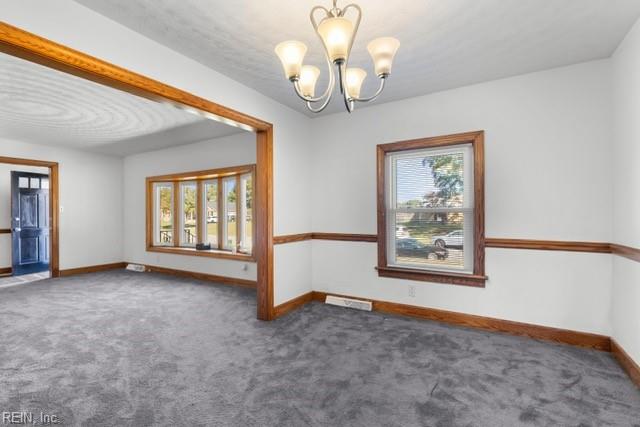 empty room featuring a wealth of natural light, a chandelier, and dark carpet