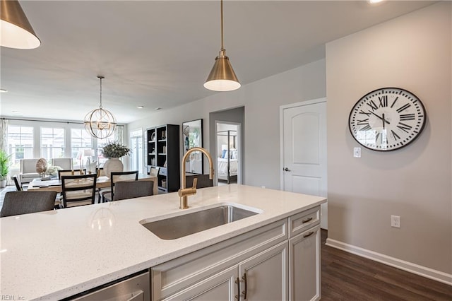 kitchen with pendant lighting, sink, light stone counters, and dark wood-type flooring