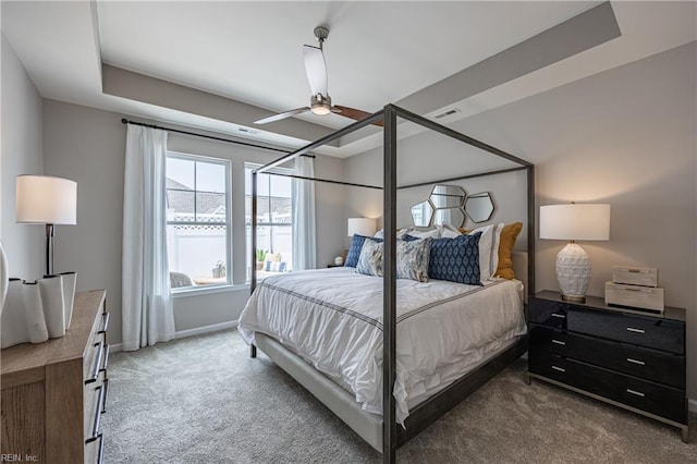 carpeted bedroom with ceiling fan and a tray ceiling