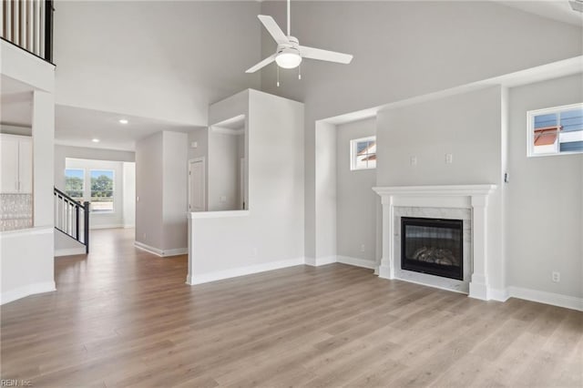 unfurnished living room featuring ceiling fan, high vaulted ceiling, light hardwood / wood-style flooring, and a high end fireplace