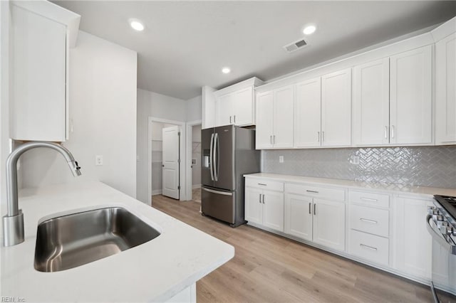 kitchen with a sink, stainless steel appliances, vaulted ceiling, light wood-style flooring, and white cabinetry
