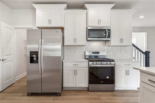 kitchen featuring white cabinets, stainless steel appliances, light wood-type flooring, and tasteful backsplash