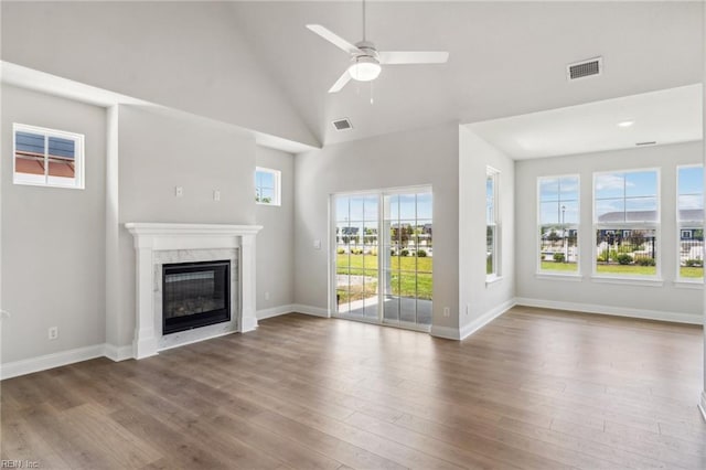 unfurnished living room with ceiling fan, a premium fireplace, a wealth of natural light, and hardwood / wood-style floors