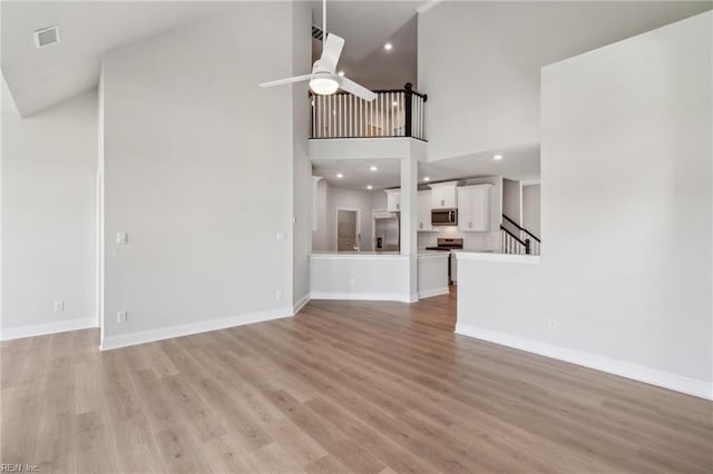 unfurnished living room featuring light hardwood / wood-style floors, a towering ceiling, and ceiling fan