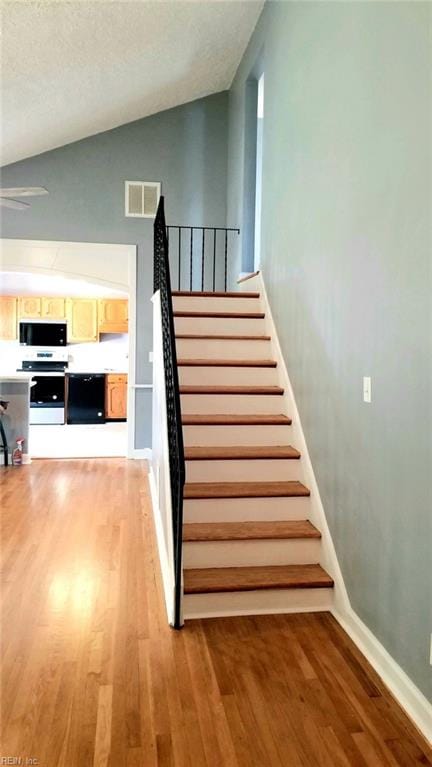 staircase featuring hardwood / wood-style floors, lofted ceiling, and a textured ceiling